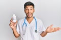 Young handsome man wearing doctor uniform holding presciption pills celebrating achievement with happy smile and winner expression