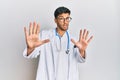 Young handsome man wearing doctor uniform and stethoscope afraid and terrified with fear expression stop gesture with hands,