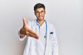 Young handsome man wearing doctor uniform and stethoscope smiling friendly offering handshake as greeting and welcoming Royalty Free Stock Photo