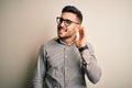 Young handsome man wearing elegant shirt and glasses over isolated white background smiling with hand over ear listening an Royalty Free Stock Photo