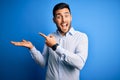 Young handsome man wearing elegant shirt standing over isolated blue background amazed and smiling to the camera while presenting Royalty Free Stock Photo