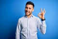 Young handsome man wearing elegant shirt standing over isolated blue background smiling positive doing ok sign with hand and Royalty Free Stock Photo