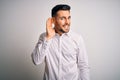 Young handsome man wearing elegant shirt standing over isolated white background smiling with hand over ear listening an hearing Royalty Free Stock Photo