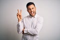 Young handsome man wearing elegant shirt standing over isolated white background smiling with happy face winking at the camera Royalty Free Stock Photo