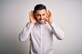 Young handsome man wearing elegant shirt standing over isolated white background Trying to hear both hands on ear gesture, curious Royalty Free Stock Photo