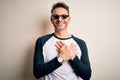 Young handsome man wearing funny thug life sunglasses meme over white background smiling with hands on chest with closed eyes and