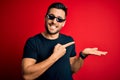 Young handsome man wearing funny thug life sunglasses over isolated red background amazed and smiling to the camera while Royalty Free Stock Photo