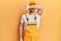 Young handsome man wearing handyman uniform over yellow background covering eyes with arm, looking serious and sad