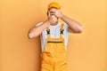 Young handsome man wearing handyman uniform over yellow background covering eyes and mouth with hands, surprised and shocked