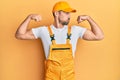 Young handsome man wearing handyman uniform over yellow background showing arms muscles smiling proud