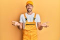 Young handsome man wearing handyman uniform over yellow background smiling cheerful with open arms as friendly welcome, positive Royalty Free Stock Photo