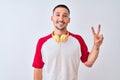 Young handsome man wearing headphones over isolated background smiling with happy face winking at the camera doing victory sign Royalty Free Stock Photo