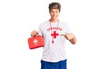 Young handsome man wearing lifeguard t shirt holding first aid kit smiling happy pointing with hand and finger