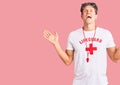 Young handsome man wearing lifeguard t shirt and whistle celebrating mad and crazy for success with arms raised and closed eyes