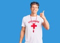 Young handsome man wearing lifeguard t shirt and whistle smiling happy and positive, thumb up doing excellent and approval sign