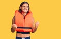 Young handsome man wearing nautical lifejacket very happy and excited doing winner gesture with arms raised, smiling and screaming Royalty Free Stock Photo