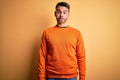 Young handsome man wearing orange casual sweater standing over isolated yellow background puffing cheeks with funny face Royalty Free Stock Photo