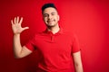 Young handsome man wearing red casual polo standing over isolated background showing and pointing up with fingers number five