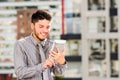 Young handsome man wearing shirt and tie standing on rooftop, holding tablet staring at screen, city buildings Royalty Free Stock Photo