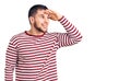 Young handsome man wearing striped sweater very happy and smiling looking far away with hand over head Royalty Free Stock Photo