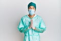 Young handsome man wearing surgeon uniform and medical mask begging and praying with hands together with hope expression on face