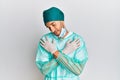Young handsome man wearing surgeon uniform and medical mask hugging oneself happy and positive, smiling confident Royalty Free Stock Photo