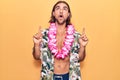 Young handsome man wearing swimwear and hawaiian lei amazed and surprised looking up and pointing with fingers and raised arms Royalty Free Stock Photo