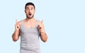 Young handsome man wearing swimwear and sleeveless t-shirt amazed and surprised looking up and pointing with fingers and raised Royalty Free Stock Photo