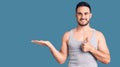 Young handsome man wearing swimwear and sleeveless t-shirt showing palm hand and doing ok gesture with thumbs up, smiling happy Royalty Free Stock Photo