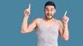 Young handsome man wearing swimwear and sleeveless t-shirt smiling amazed and surprised and pointing up with fingers and raised Royalty Free Stock Photo