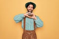 Young handsome man wearing tratidional german octoberfest custome for Germany festival smiling in love doing heart symbol shape