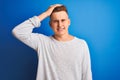 Young handsome man wearing white casual t-shirt standing over isolated blue background stressed with hand on head, shocked with Royalty Free Stock Photo