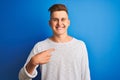 Young handsome man wearing white casual t-shirt standing over isolated blue background with surprise face pointing finger to Royalty Free Stock Photo