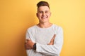 Young handsome man wearing white casual t-shirt standing over isolated yellow background happy face smiling with crossed arms Royalty Free Stock Photo