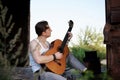 Young handsome man, wearing white t-shirt and grey pants, sitting inside old railway carriage, playing guitar, composing music