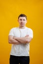 Young handsome man wearing white t-shirt with happy face smiling with crossed arms looking at the camera over yellow studio Royalty Free Stock Photo