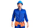 Young handsome man wearing worker uniform and hardhat afraid and shocked, surprise and amazed expression with hands on face Royalty Free Stock Photo