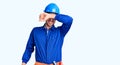 Young handsome man wearing worker uniform and hardhat covering eyes with arm smiling cheerful and funny