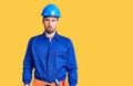 Young handsome man wearing worker uniform and hardhat crazy and scared with hands on head, afraid and surprised of shock with open Royalty Free Stock Photo