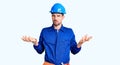 Young handsome man wearing worker uniform and hardhat doing bunny ears gesture with hands palms looking cynical and skeptical Royalty Free Stock Photo