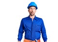 Young handsome man wearing worker uniform and hardhat making fish face with lips, crazy and comical gesture Royalty Free Stock Photo
