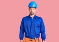 Young handsome man wearing worker uniform and hardhat in shock face, looking skeptical and sarcastic, surprised with open mouth Royalty Free Stock Photo