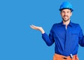 Young handsome man wearing worker uniform and hardhat smiling showing both hands open palms, presenting and advertising comparison Royalty Free Stock Photo