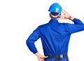 Young handsome man wearing worker uniform and hardhat standing backwards looking away with crossed arms