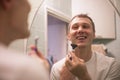 Young handsome man in white t-shirt shaves in front of bathroom mirror in the morning. Royalty Free Stock Photo