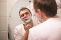 Young handsome man in white t-shirt shaves in front of bathroom mirror in the morning. Royalty Free Stock Photo