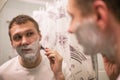 Young handsome man in white t-shirt shaves in front of bathroom mirror in the morning. Royalty Free Stock Photo