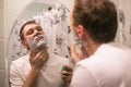 Young handsome man in white t-shirt shaves in front of bathroom mirror in the morning. Royalty Free Stock Photo