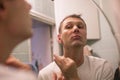 Young handsome man in white t-shirt shaves in front of bathroom mirror in the morning. Royalty Free Stock Photo