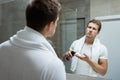 Young handsome man with white towel on his shoulders looking in the bathroom mirror putting shaving foam on his hand Royalty Free Stock Photo